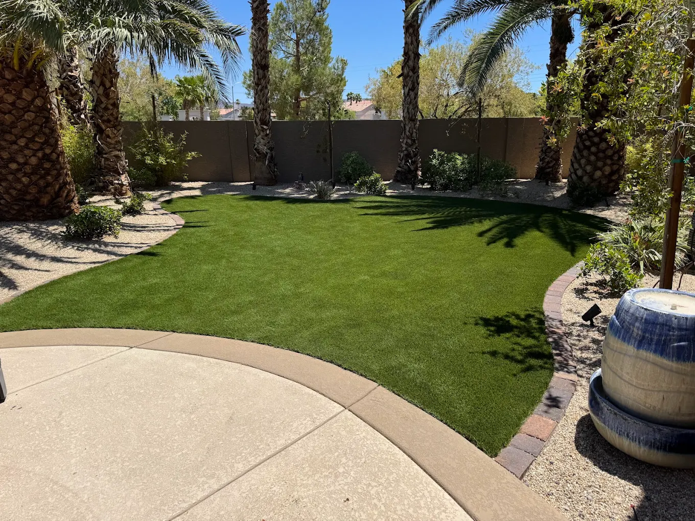 Lush green artificial turf in a Henderson backyard with curved landscaping borders and palm trees